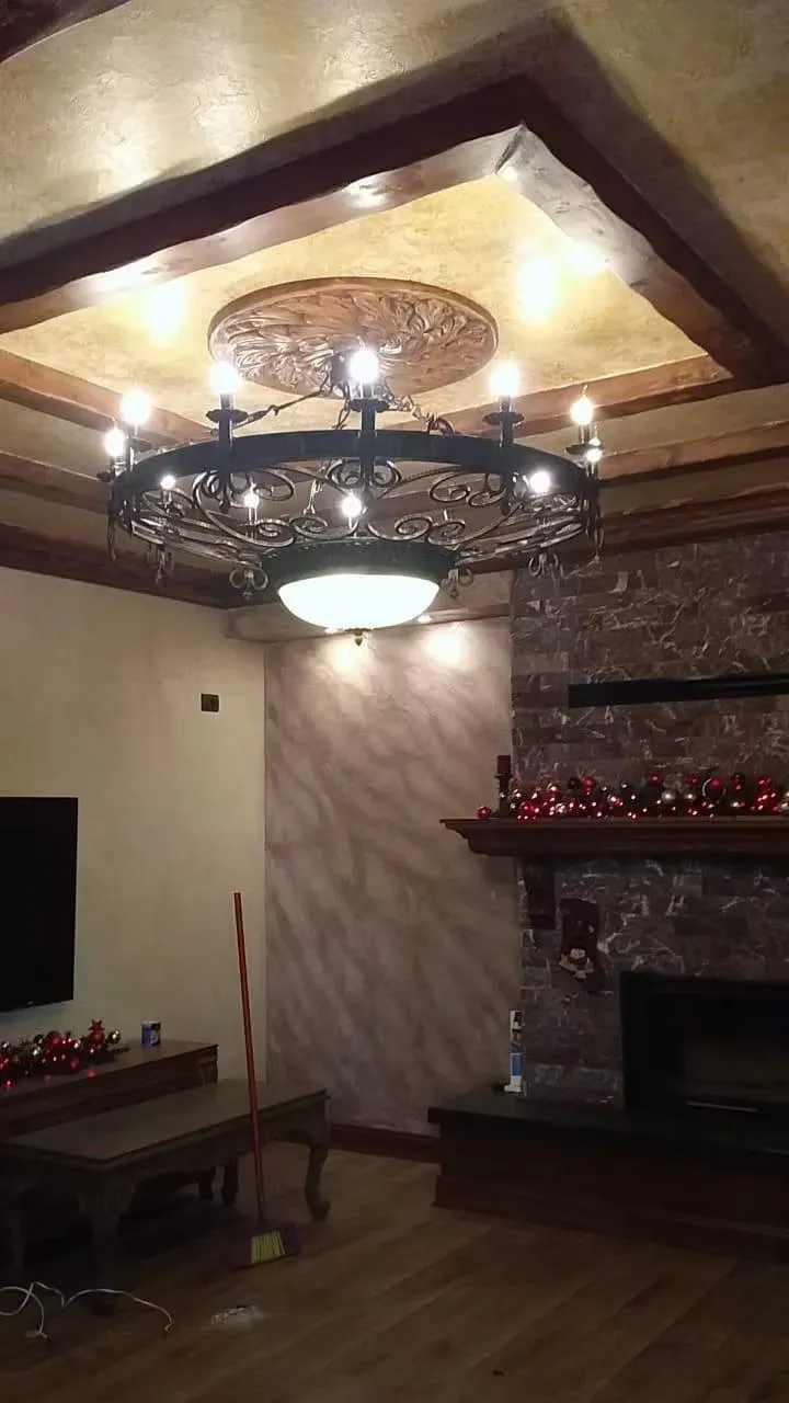 Large hand-forged iron ring chandelier with scrollwork and candle arms in a living room